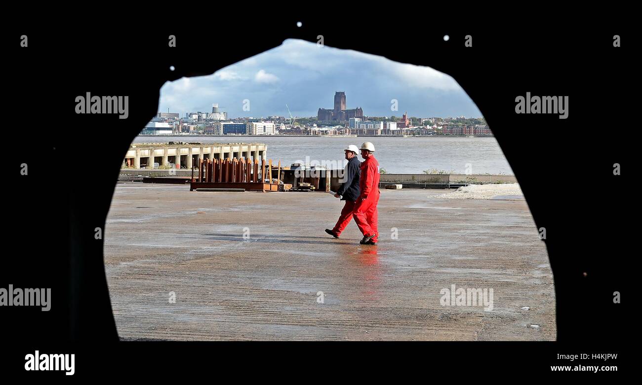 Deux employés de Cammell Laird's ship builders à Birkenhead, sont vus à travers un trou dans le mur du chantier. Banque D'Images