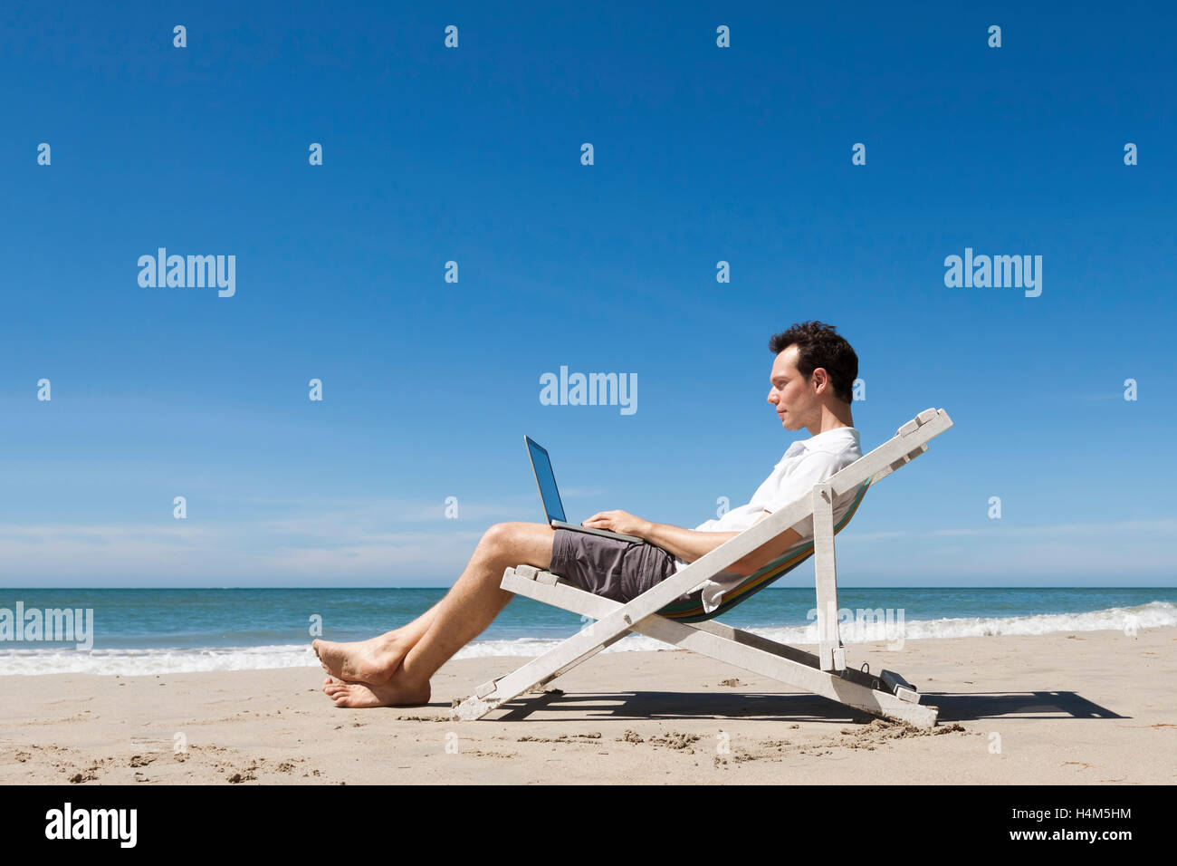 Jeune indépendant travaillant en ligne avec ordinateur portable sur une plage tropicale ensoleillée Banque D'Images