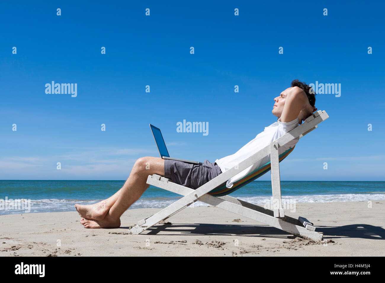 Homme d'affaires prospère reposant sur une plage tropicale avec portable Banque D'Images