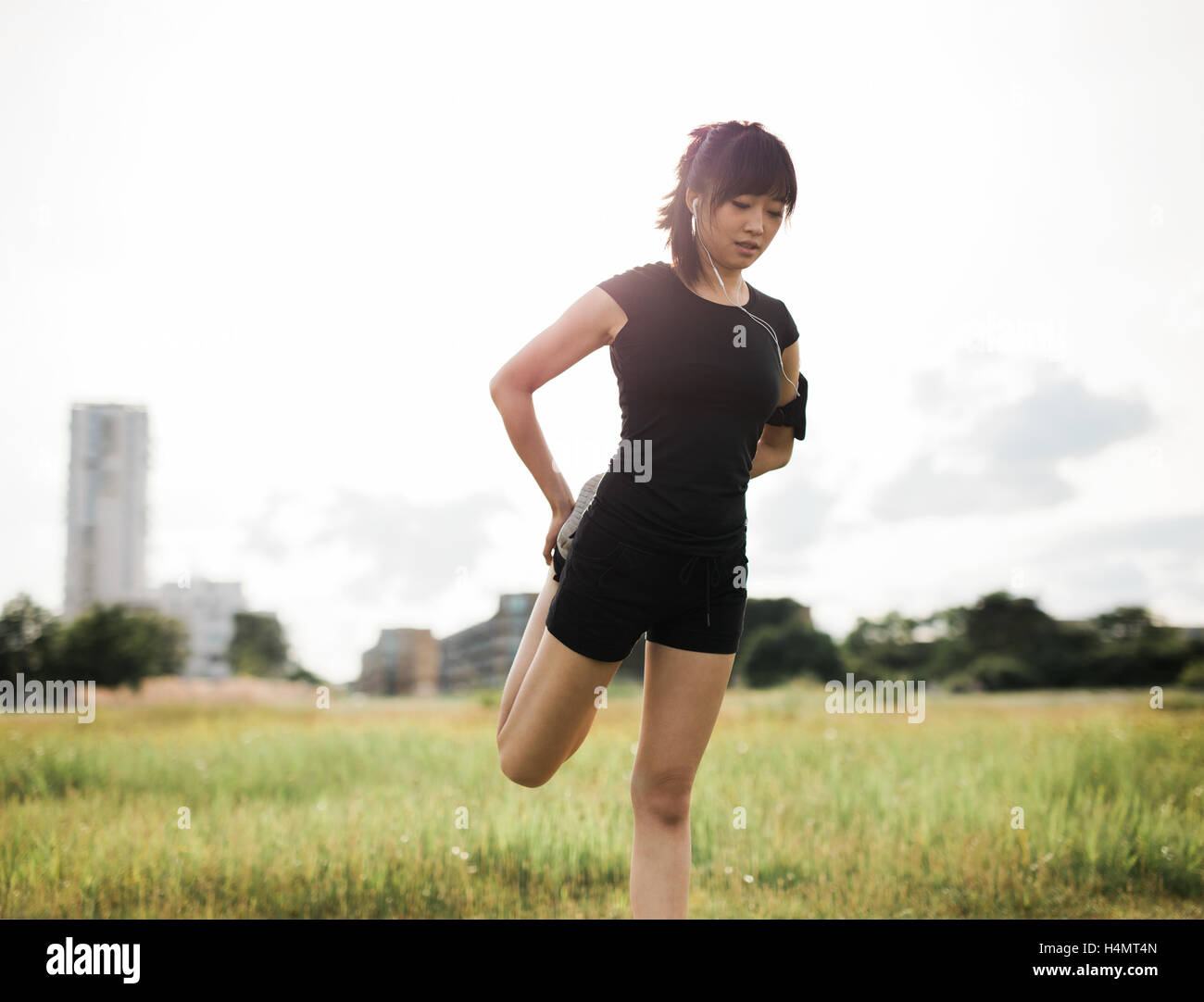 Shot de fit young woman stretching ses jambes au parc urbain. Modèle féminin en chinois sportswear faire réchauffer l'exercice dans un parc en Banque D'Images