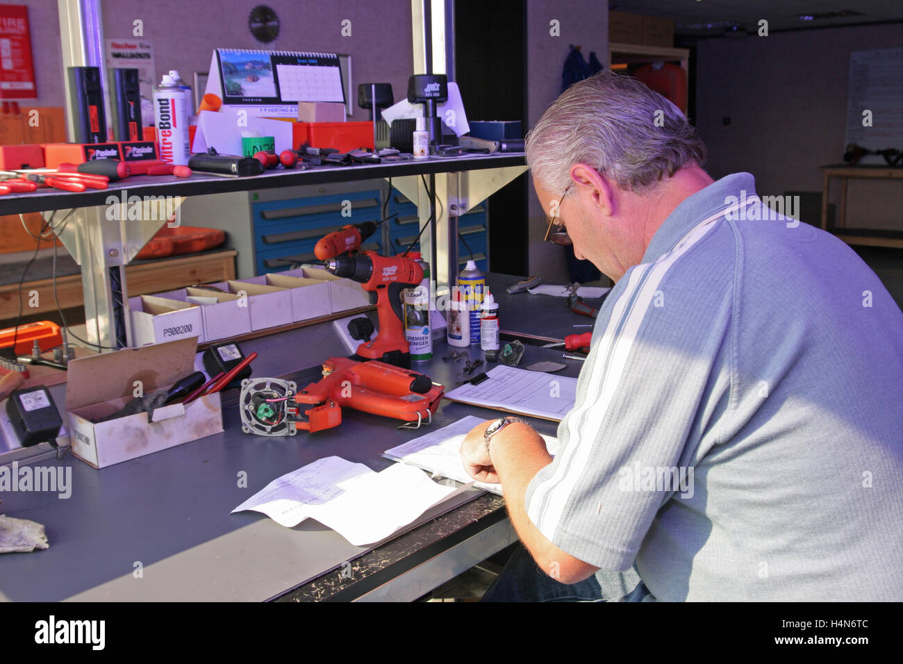 Un ingénieur d'âge moyen prend des notes qu'il répare et services des outils électriques à un établi Banque D'Images