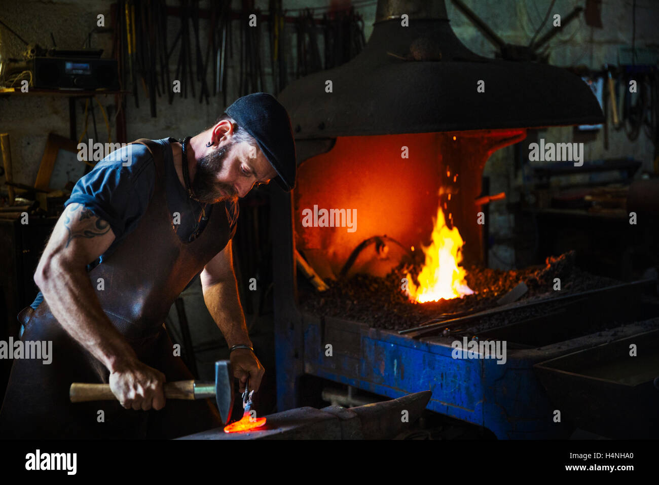 Un forgeron frappe un morceaux de métal chaud rouge sur l'enclume avec un marteau dans un atelier. Banque D'Images