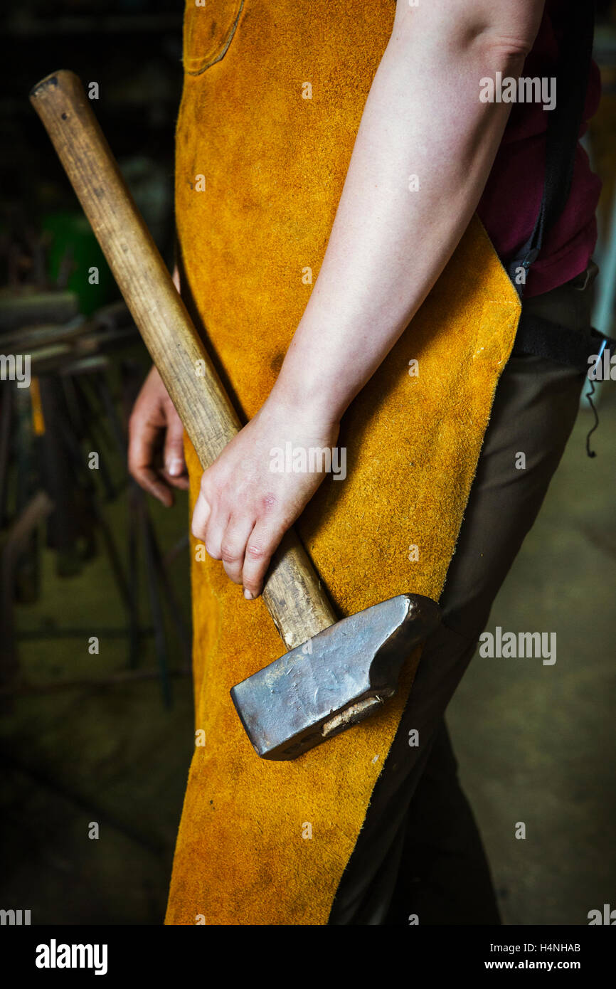Un forgeron dans un tablier résistant à la tenue d'un gros marteau. Banque D'Images
