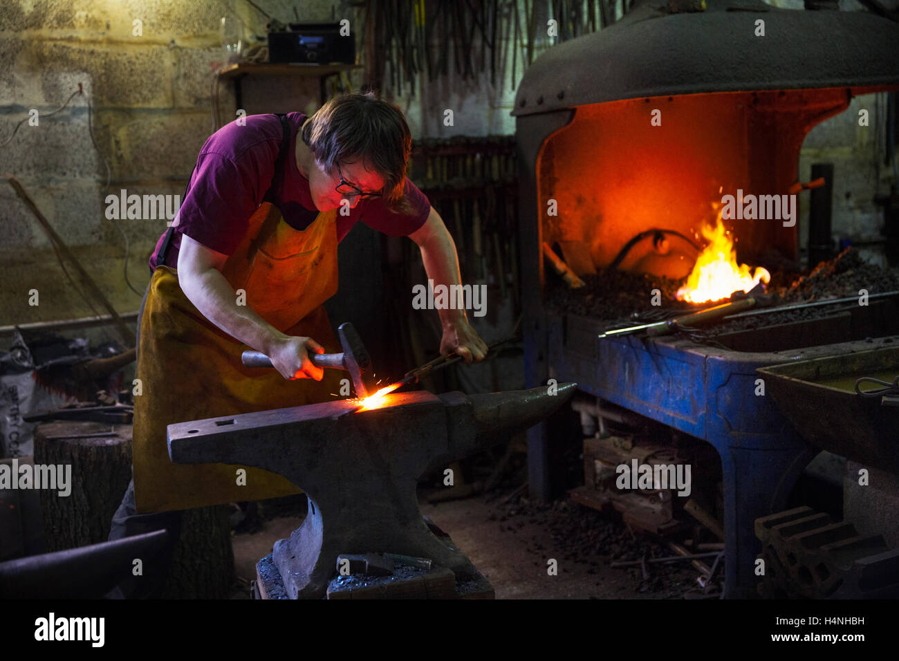 Un forgeron d'un rouge pourpre le métal chaud sur enclume à l'intérieur d'un atelier. Banque D'Images