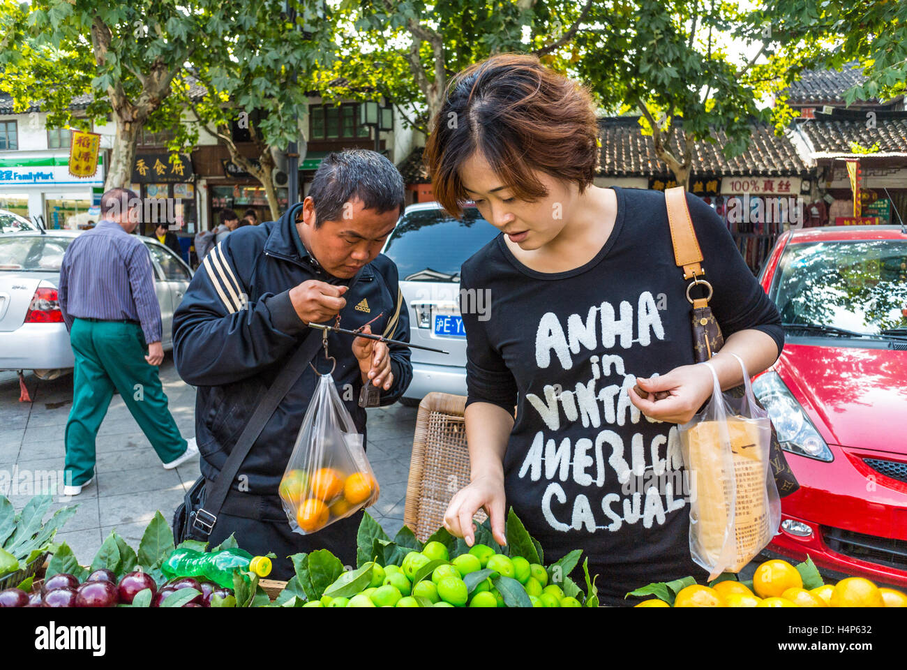 Vente, shopping et personnes concept - jeune femme chinoise choisir les fruits mûrs à street Banque D'Images