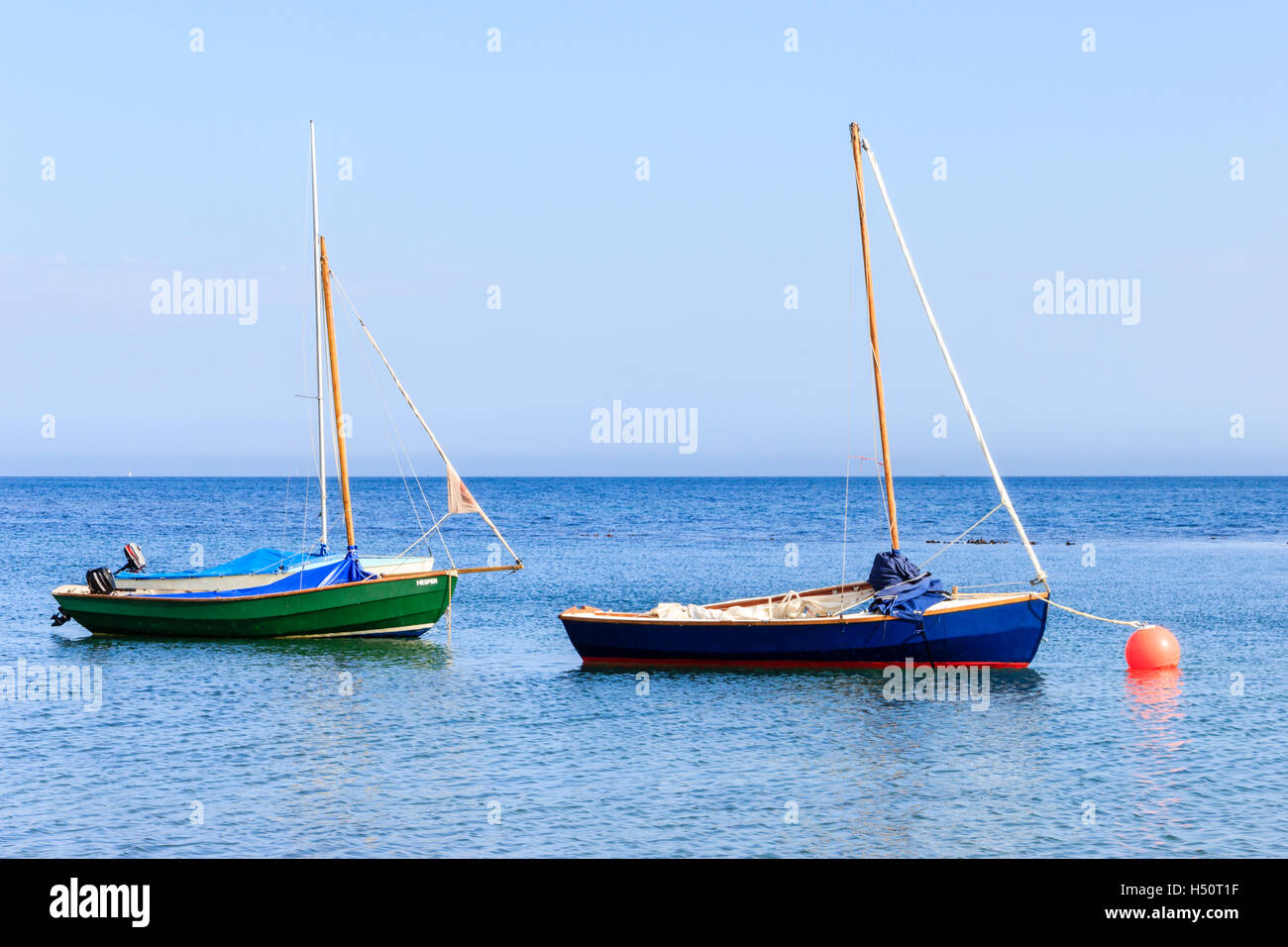 Deux petits mâts de voiliers, l'un vert bleu, ancrée sur une mer calme à Ringstead Bay, Dorset, England, UK, un amarré à une bouée orange Banque D'Images