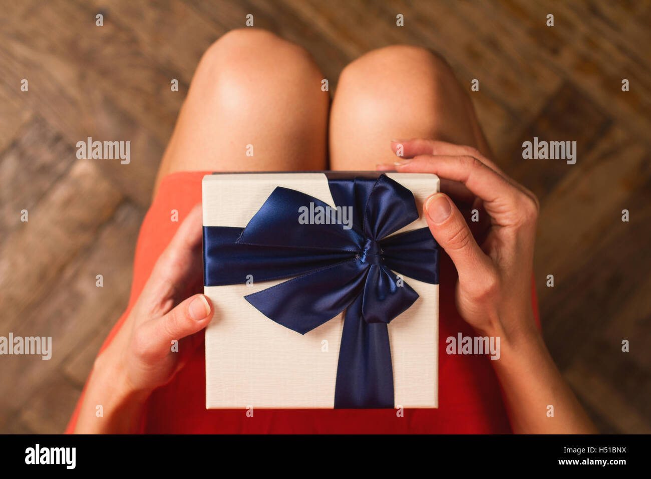 Vue supérieure de la femme avec robe rouge tenant une boîte-cadeau avec ruban bleu sur ses genoux Banque D'Images