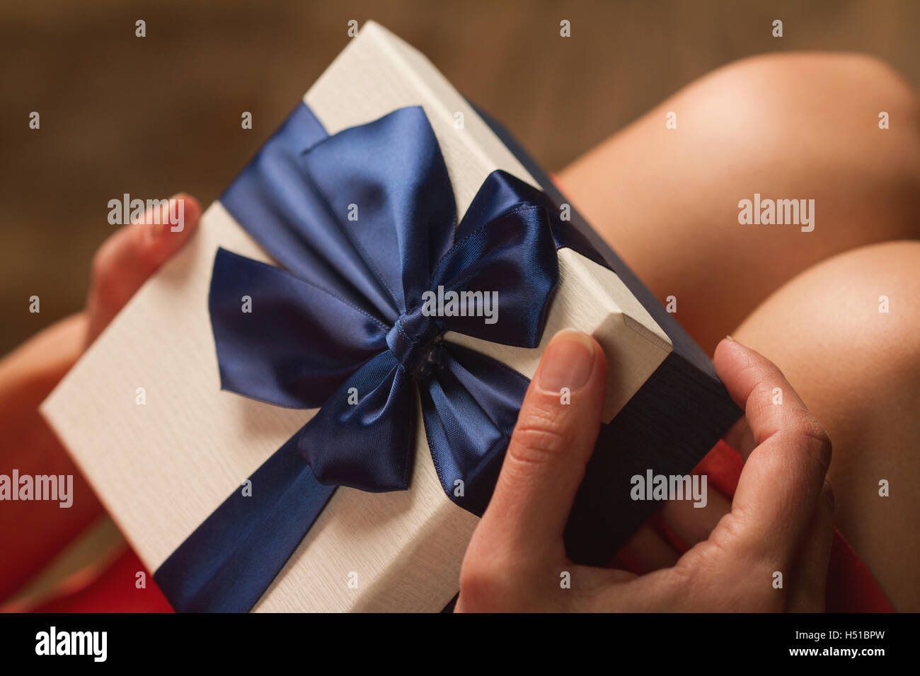 Vue de côté de femme avec robe rouge tenant une boîte-cadeau avec ruban bleu sur ses genoux Banque D'Images