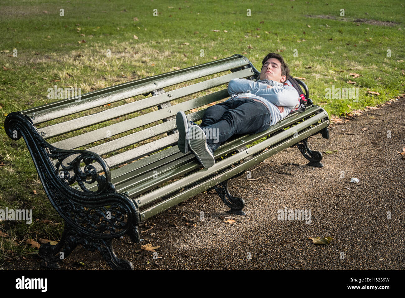 Un jeune homme endormi sur un banc de parc dans un parc de Londres Banque D'Images