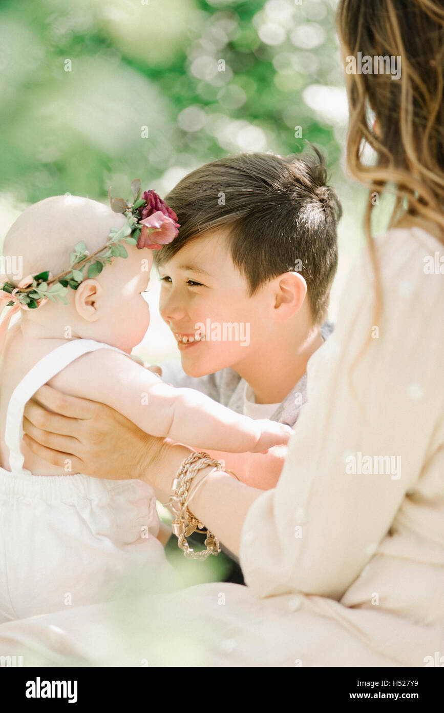 Une femme, un garçon et une petite fille avec une couronne de fleurs sur la tête, assis dans un jardin. Banque D'Images