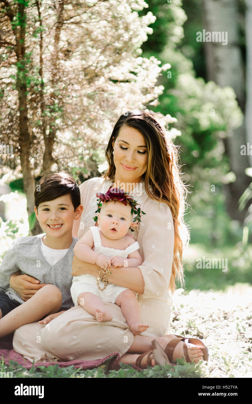 Portrait of a smiling mother, garçon et fille avec une couronne de fleurs sur la tête, assis dans un jardin. Banque D'Images