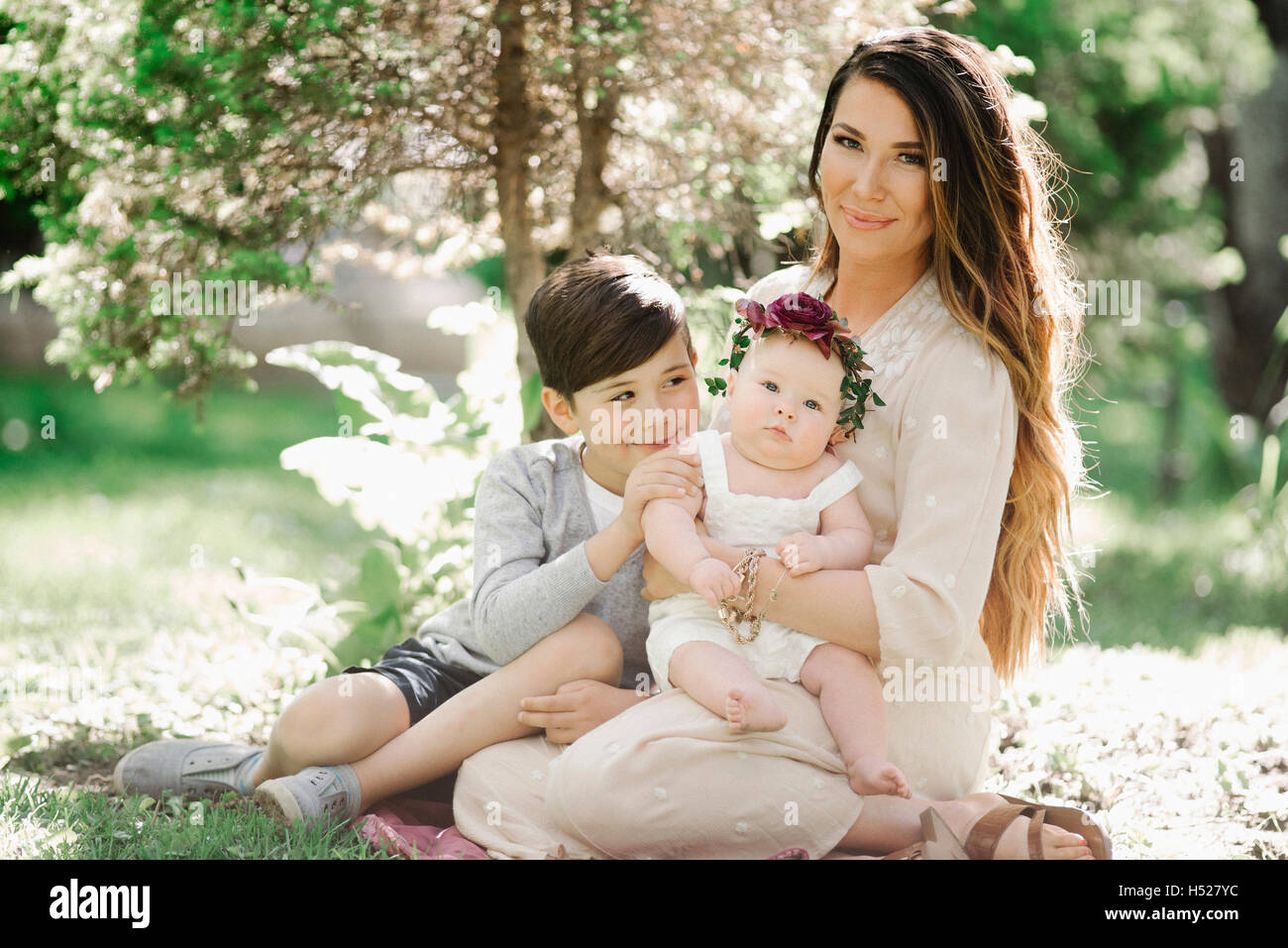 Portrait of a smiling mother, garçon et fille avec une couronne de fleurs sur la tête, assis dans un jardin. Banque D'Images