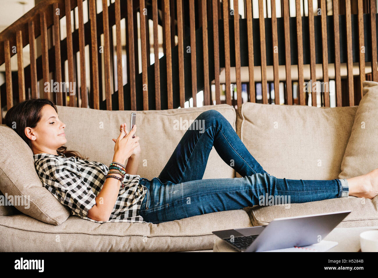 Femme aux longs cheveux brun couché sur un canapé, à l'aide d'un téléphone mobile. Banque D'Images