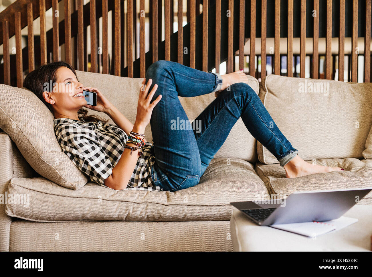 Femme aux longs cheveux brun couché sur un canapé, à l'aide d'un téléphone mobile. Banque D'Images