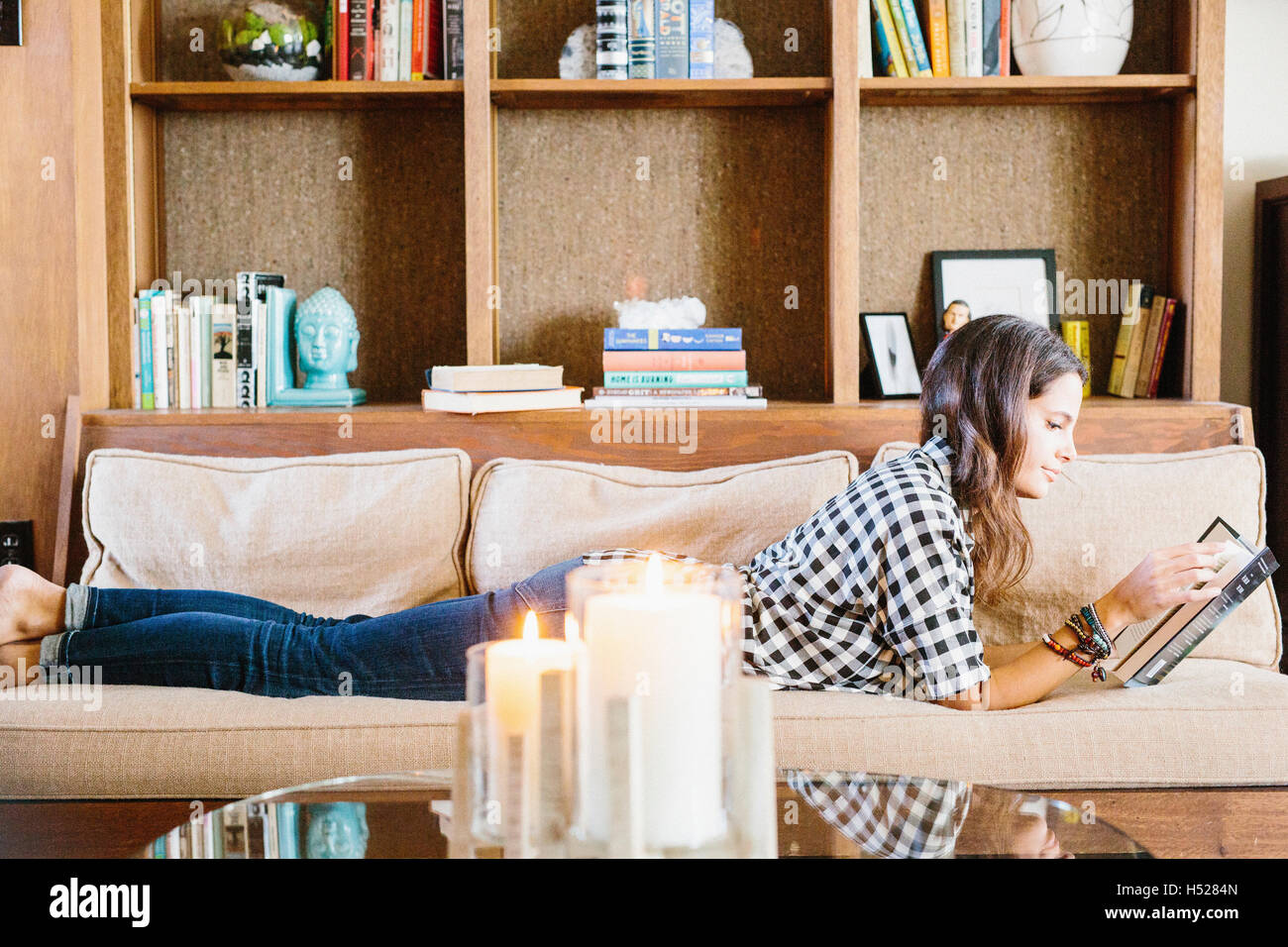 Femme aux longs cheveux brun couché sur un canapé, la lecture d'un livre. Banque D'Images