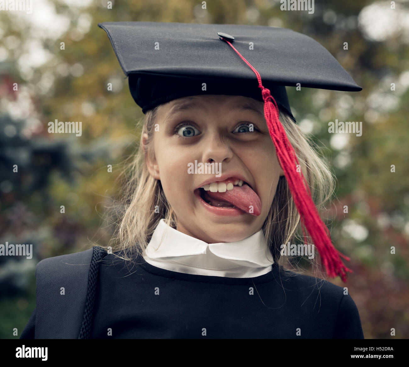 Belle fille blonde dans l'uniforme scolaire et graduation cap sur sa tête en langue maternelle comme Albert Einstein. Banque D'Images