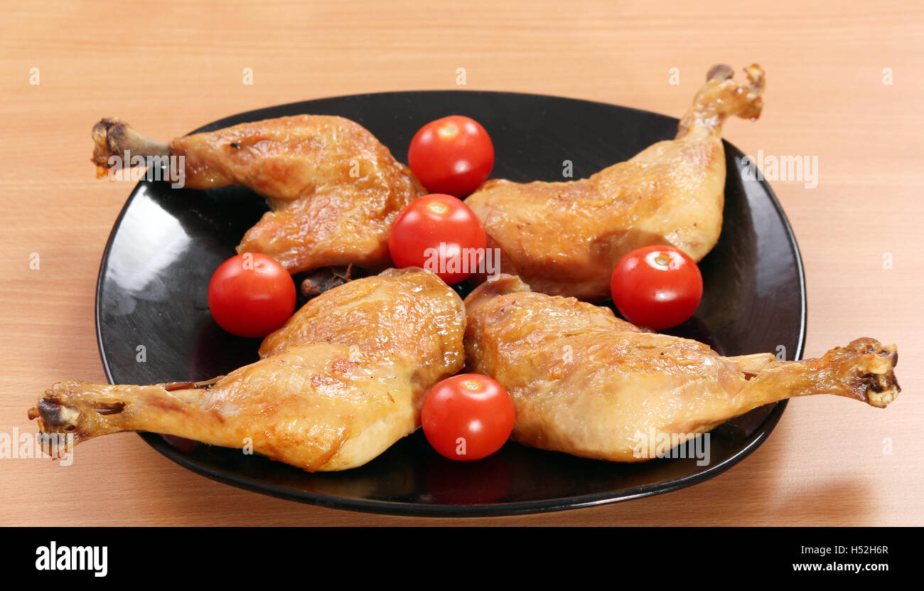 Pilons de poulet et les tomates sur le plat noir Banque D'Images