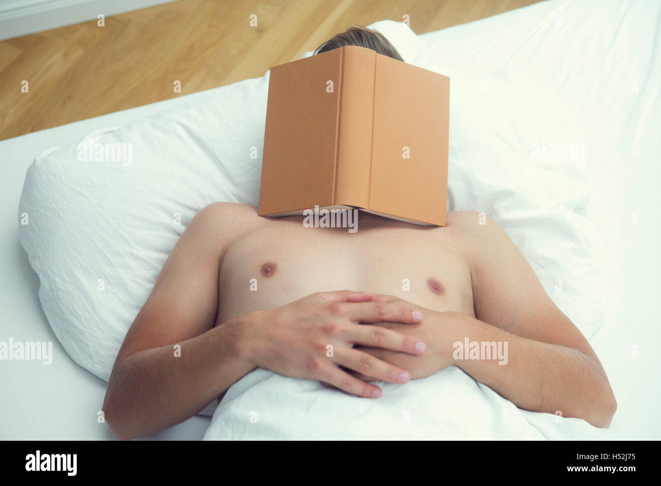 L'homme de dormir dans le lit avec des draps blancs avec un livre sur la tête Banque D'Images