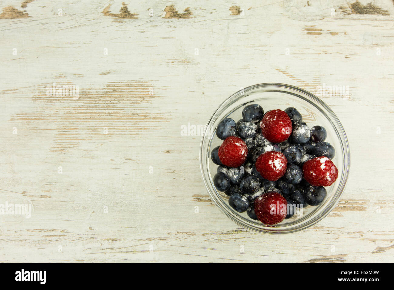 Bleuets et framboises saupoudrées de sucre glace dans un bol en verre sur une vieille table en bois clair, dans un style vintage , spa copie Banque D'Images