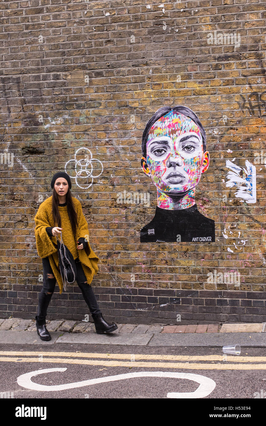 Jeune femme à côté d'une nouvelle fresque sur un mur de briques représentant le visage d'une jeune femme près de Brick Lane, Shoreditch Banque D'Images