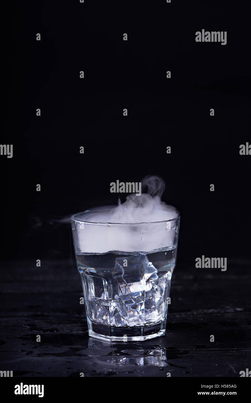 L'eau chaude avec beaucoup de vapeur dans un verre à fond noir. Photo sombre. Concept photo : trois état de l'eau - la glace, l'eau, st Banque D'Images