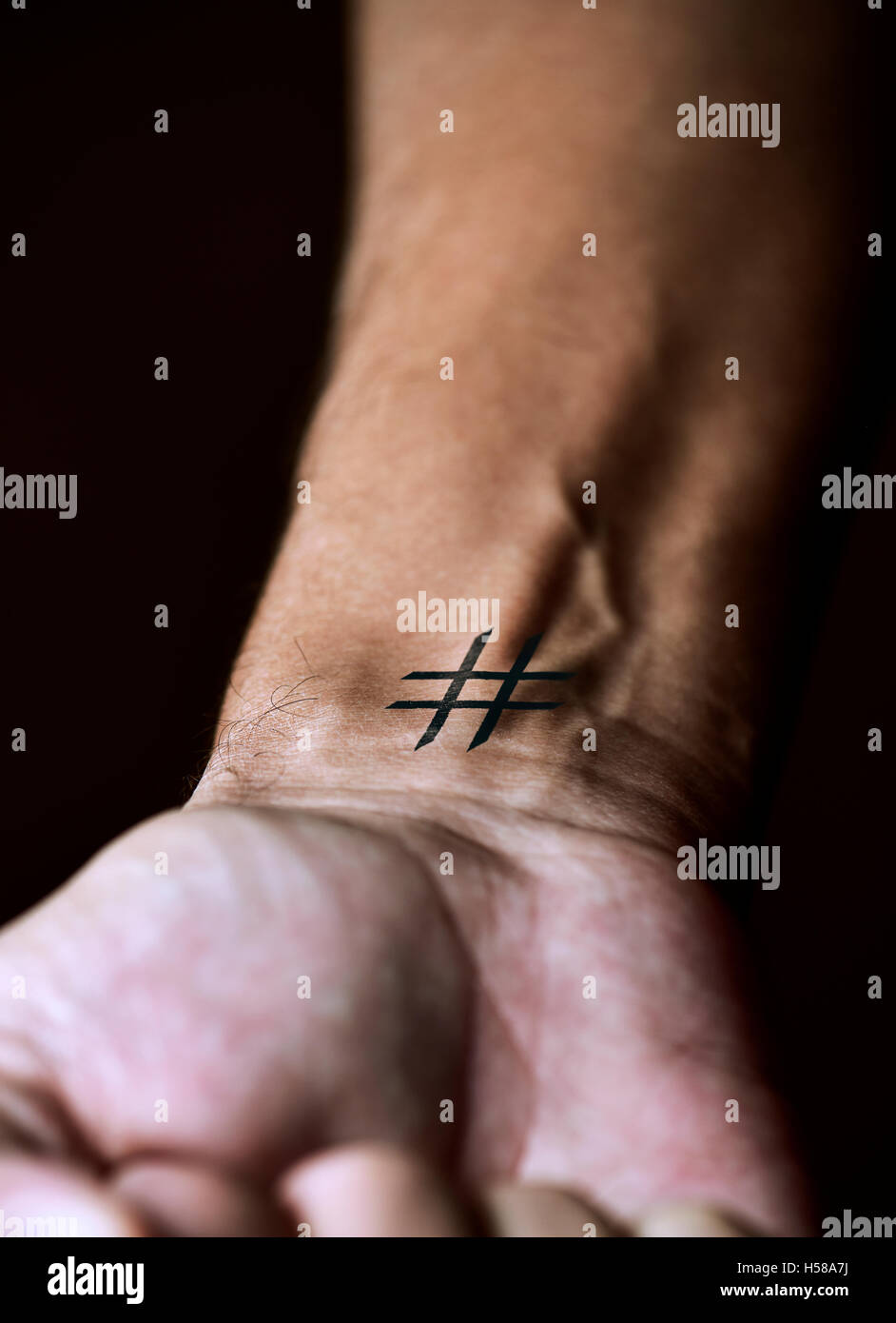 Libre d'un jeune homme de race blanche avec un dièse simulant un tatouage dans son poignet, sur un fond noir Banque D'Images