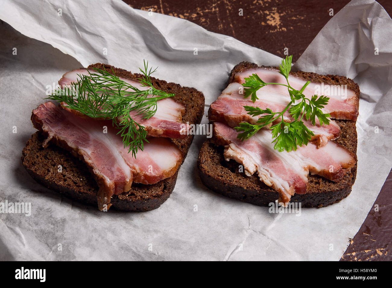 Vue rapprochée des tranches de lard fumé sur le morceau de pain de seigle avec des herbes - style rustique sur brown vintage. Banque D'Images