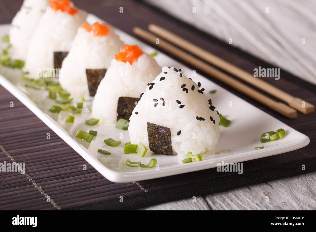 Boules de riz onigiri avec du saumon et sésame sur une assiette blanche horizontale. Banque D'Images