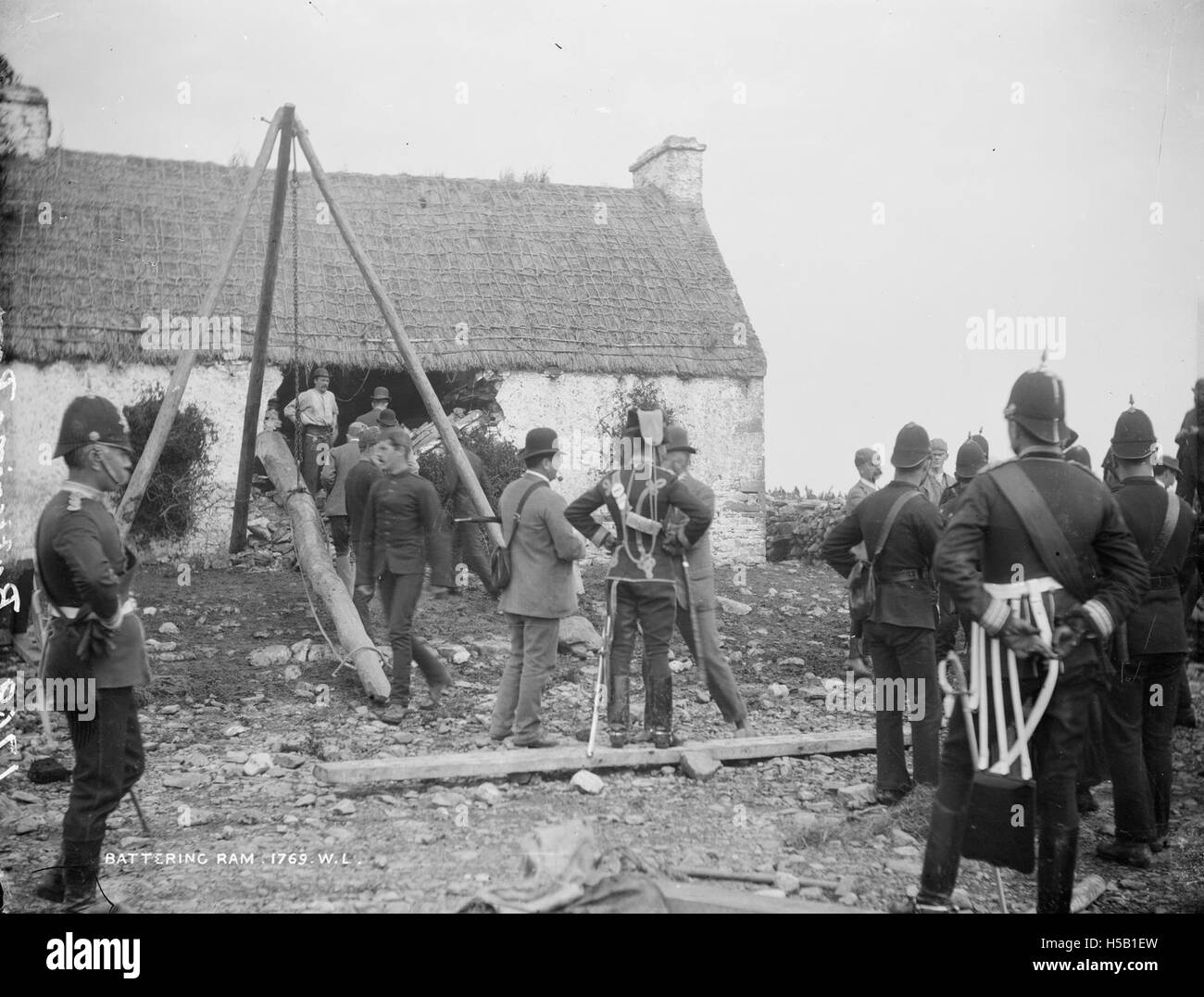L'image montre une maison à Moyasta, dans le comté de Clare, avec un bélier battant et des soldats debout à l'extérieur, suggérant une scène liée à l'armée ou à un conflit, peut-être du début du XXe siècle. La présence des soldats peut indiquer un événement historique ou une action militaire dans la région pendant cette période. Banque D'Images