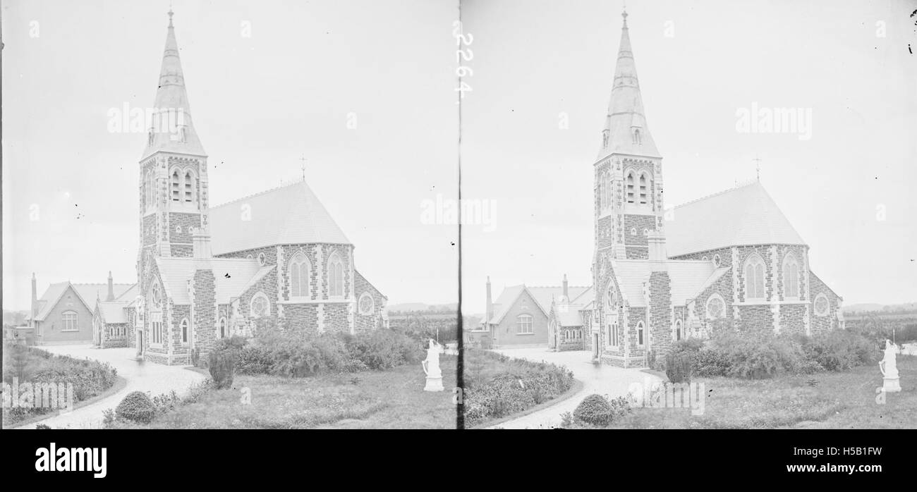 Cette photographie montre une église moderne de style gothique située en pleine campagne. L'église comporte une tour carrée et une flèche, avec une statue d'un guerrier tenant une harpe placée en évidence au premier plan, créant un contraste visuel saisissant. Banque D'Images