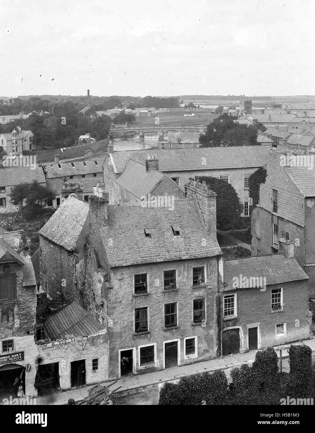 Une vue surélevée d'une ville montrant plusieurs bâtiments, dont l'un affiche bien en vue un panneau indiquant « Thomas Hart, concessionnaire maritime », suggérant une entreprise liée aux services ou produits maritimes. Banque D'Images