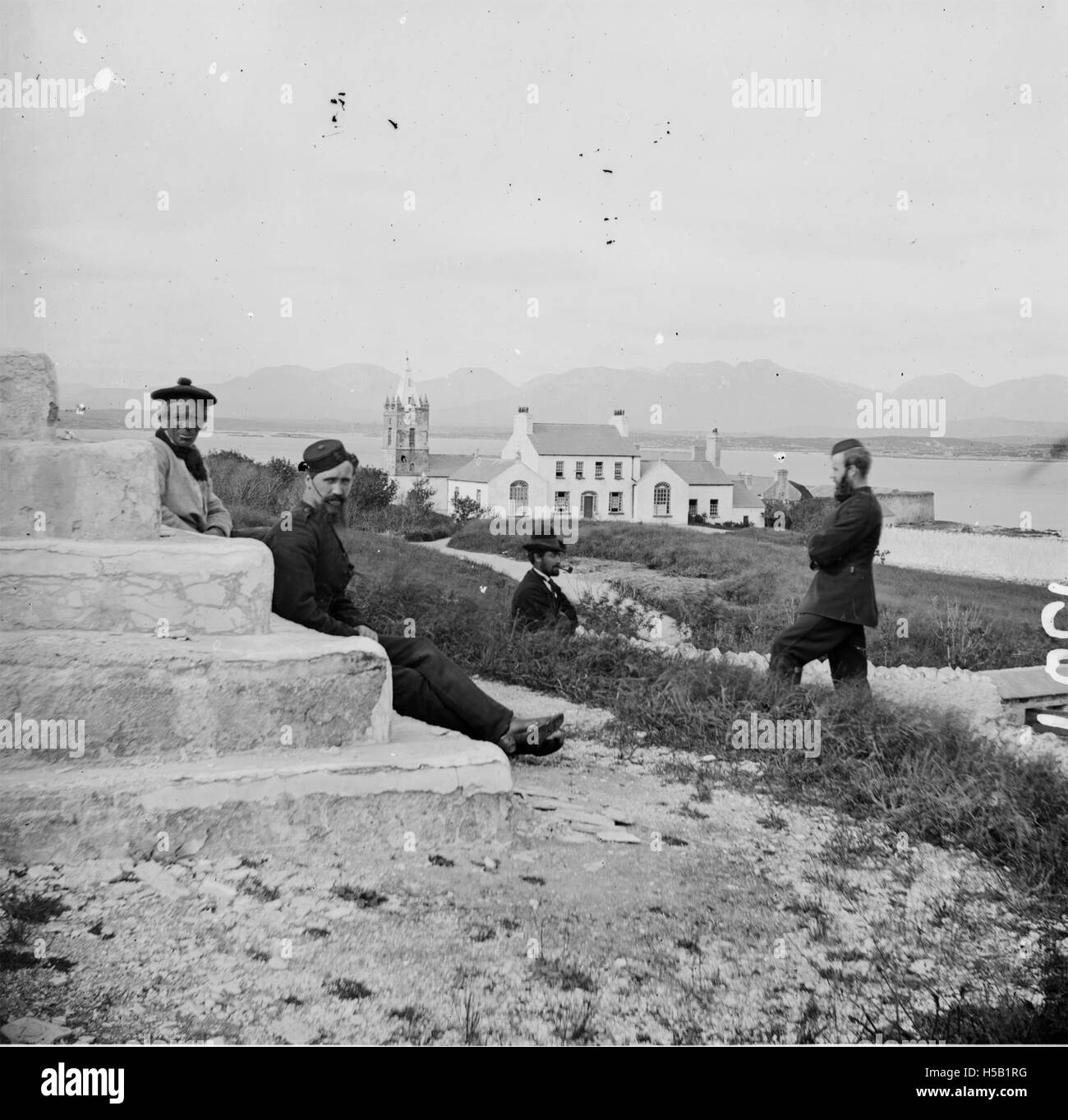 Cette image présente une vue panoramique avec une mer en arrière-plan, des collines et une église avec une flèche. Deux constables et deux autres individus sont vus sur les marches ou le socle au premier plan, suggérant une scène historique ou artistique. Banque D'Images