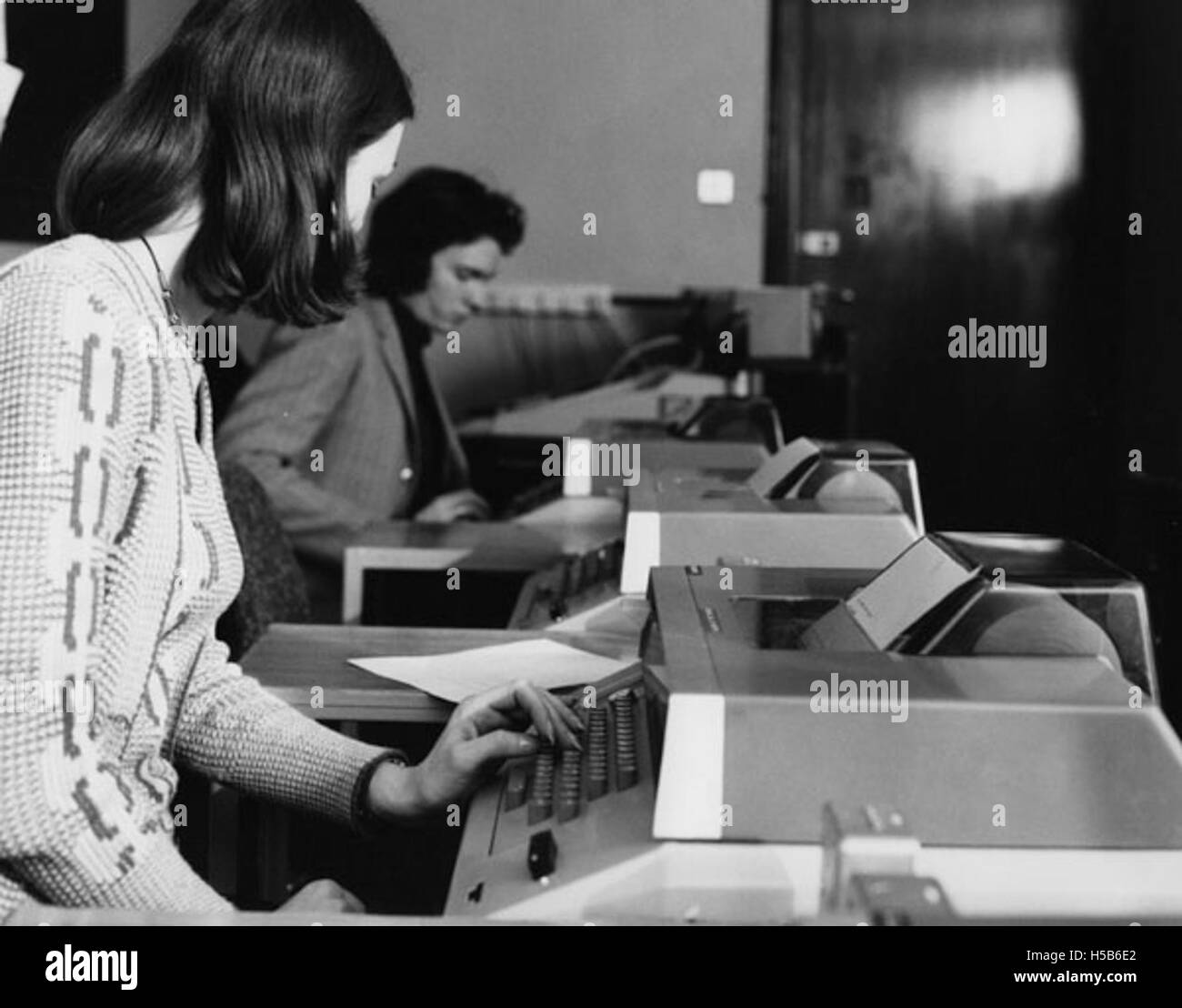 Cette photographie des années 1970 montre des étudiants dans une salle informatique, probablement dans un cadre universitaire ou collégial. L'image capture les premiers jours de l'utilisation de l'ordinateur dans l'éducation, avec des étudiants travaillant sur les premiers systèmes informatiques. Banque D'Images