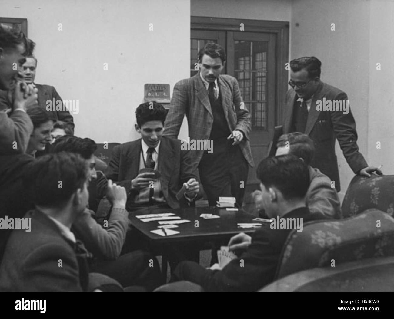 Dans cette photographie de 1951, des élèves jouent aux cartes dans l’une des salles communes, mettant en évidence les interactions sociales dans un cadre académique ou résidentiel. Cette scène reflète la vie étudiante au début des années 1950, avec des jeux de cartes servant de passe-temps commun aux pairs dans des espaces de vie partagés. Banque D'Images