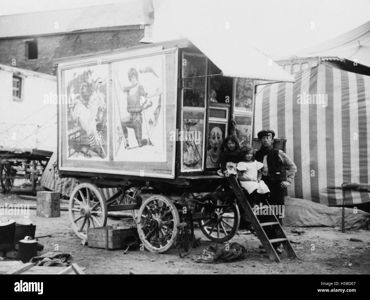 Une photographie de deux enfants et d'un homme assis sur les marches d'une caravane lors d'une représentation de 'Buff Bill's Circus', mettant en évidence les aspects culturels des cirques itinérants du début du XXe siècle. Banque D'Images