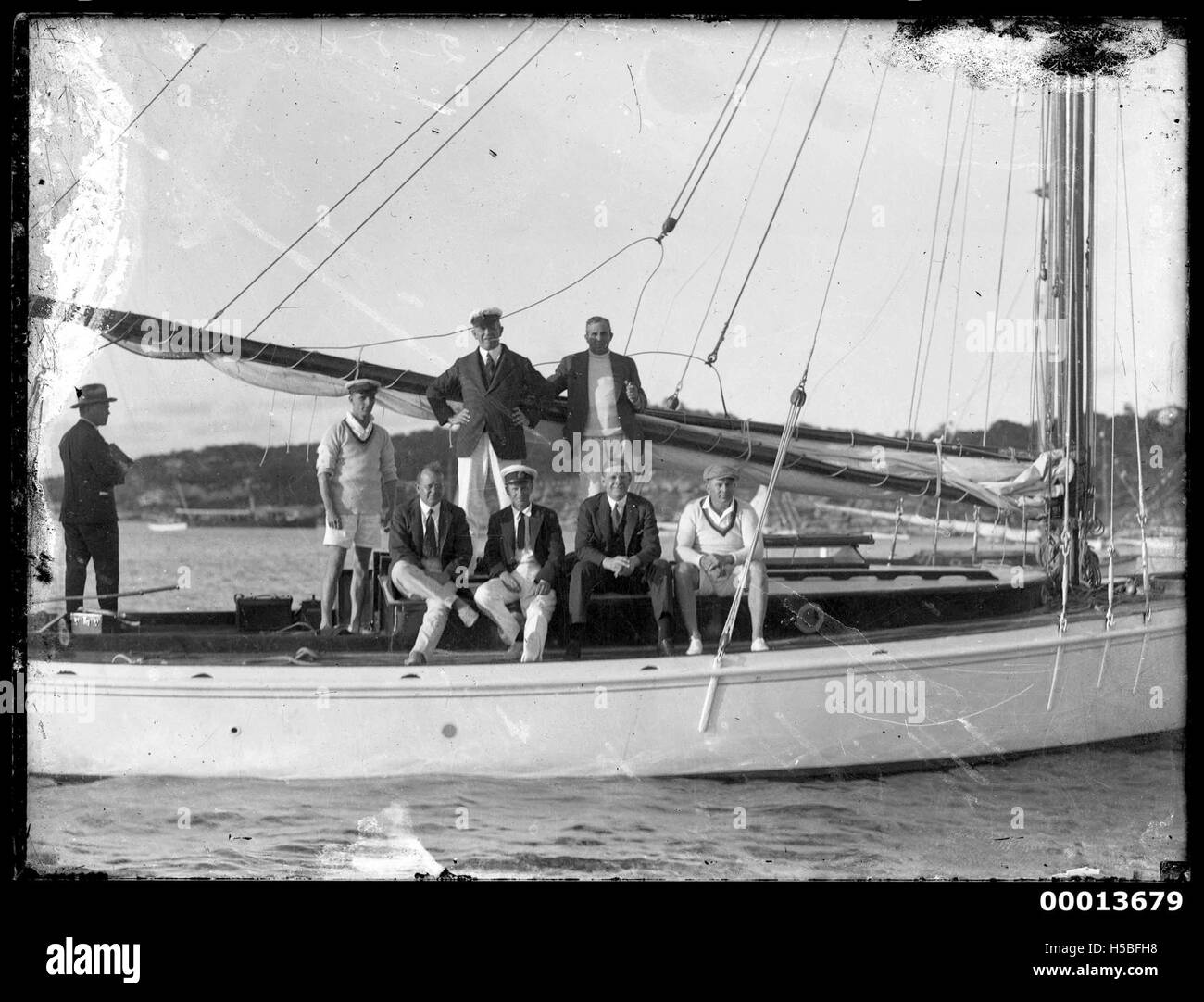 Un groupe de huit hommes est vu posant sur un bateau, capturant un moment probablement du début du XXe siècle. L'image reflète les activités sociales et la culture de la navigation de plaisance de l'époque, en particulier dans les environnements nautiques. Banque D'Images