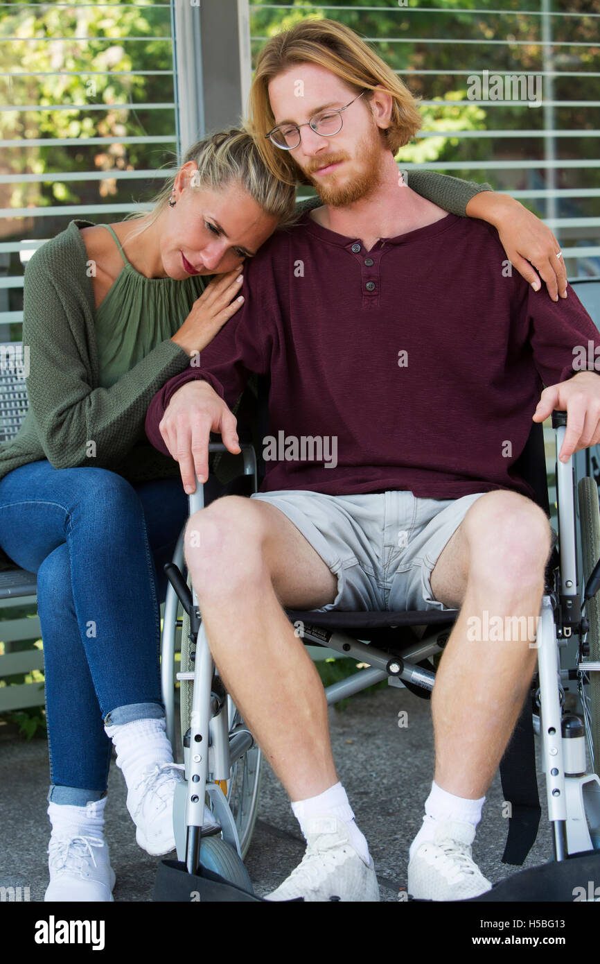 Woman hugging jeune homme en fauteuil roulant et à la triste Banque D'Images