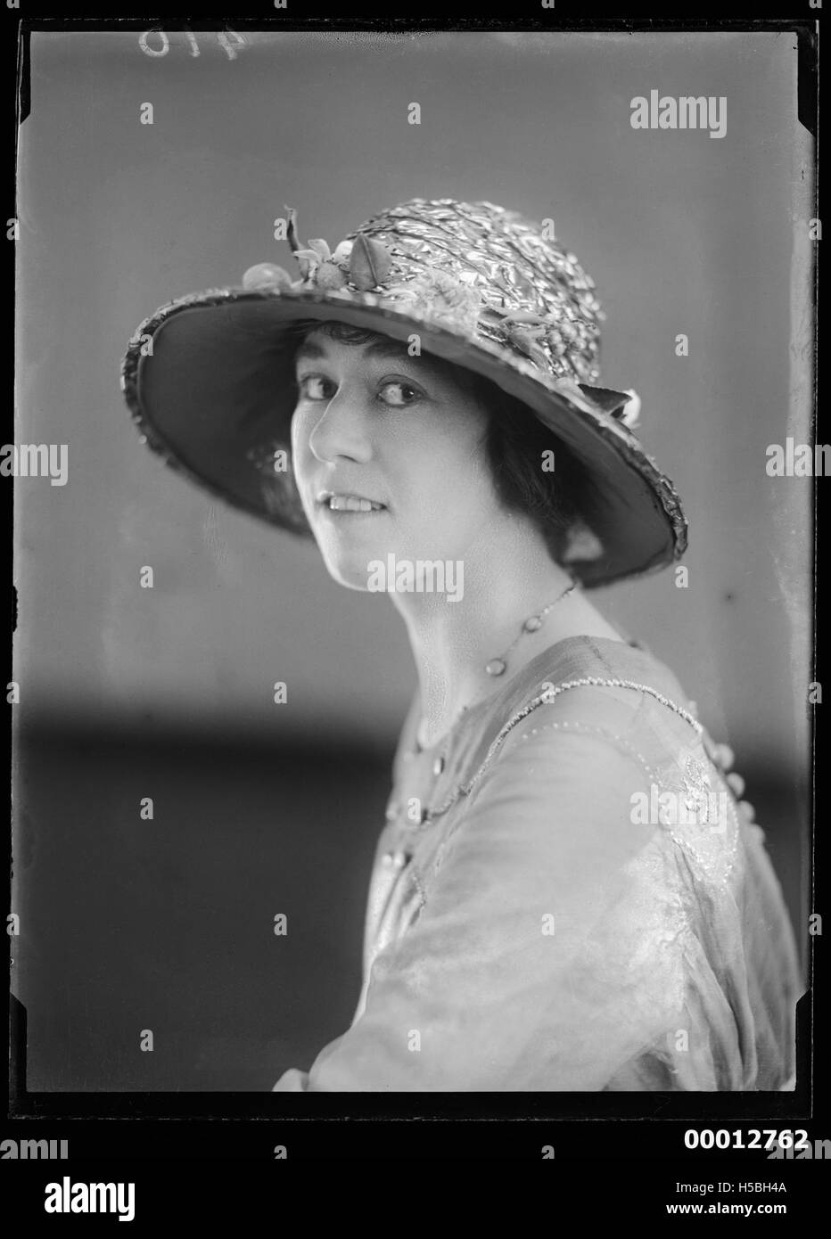 Ce portrait représente une femme non identifiée portant un chapeau. La photographie la capture dans un cadre formel, mettant en valeur sa tenue vestimentaire et son expression. Banque D'Images
