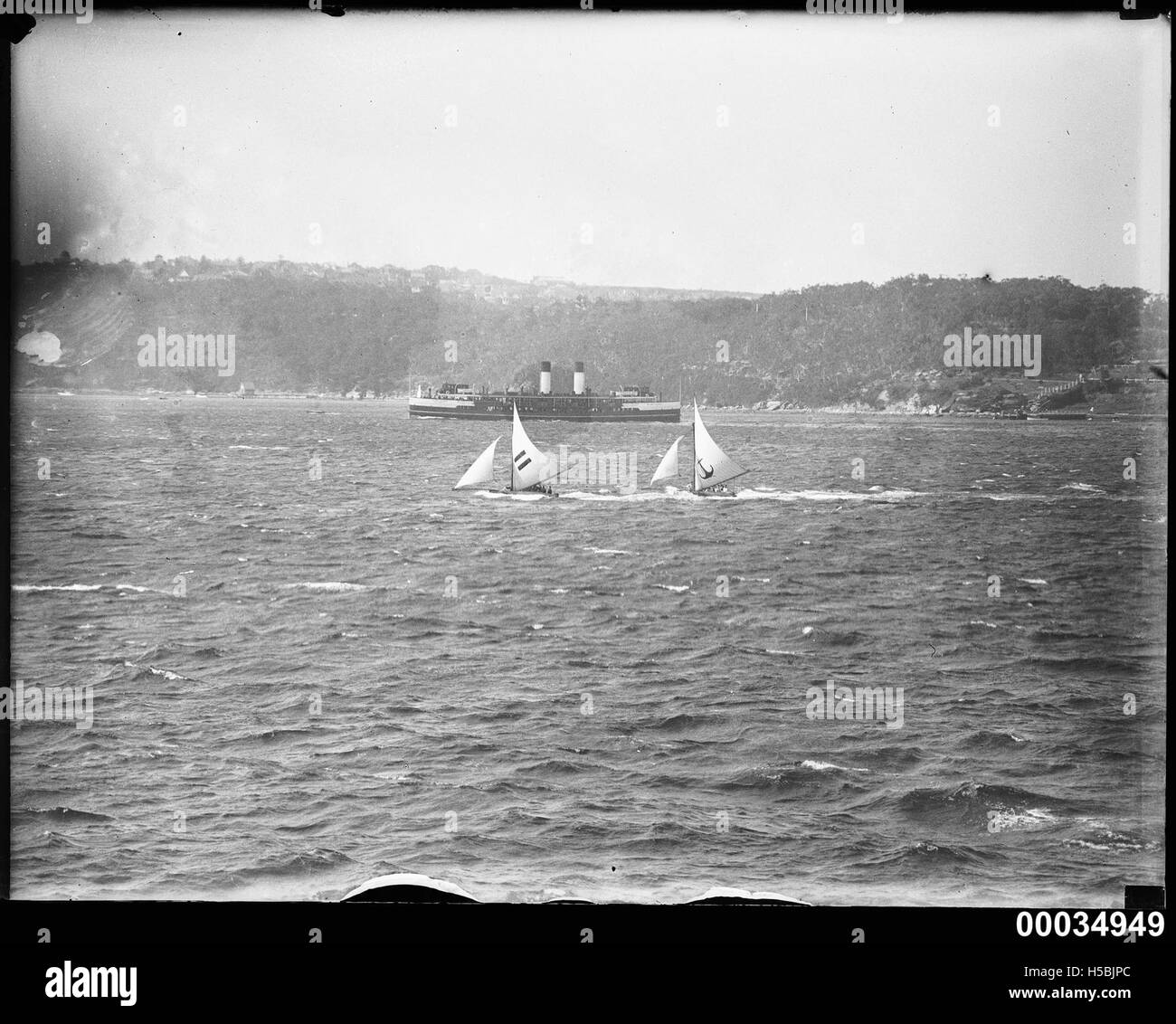 Cette photographie représente deux sloops qui courent près du CURL CURL du ferry dans le port de Sydney. L'image capture l'excitation et la nature compétitive de la voile dans l'un des ports les plus emblématiques d'Australie. Banque D'Images