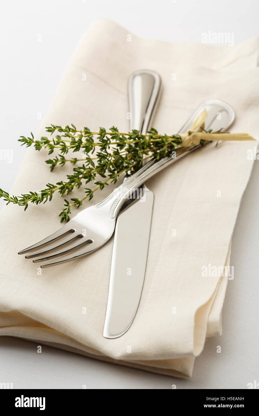 Réglage de la table simple et classique avec réglage de l'argenterie fourchettes et couteau sur serviette en lin blanc et un brin de thym herbes Banque D'Images