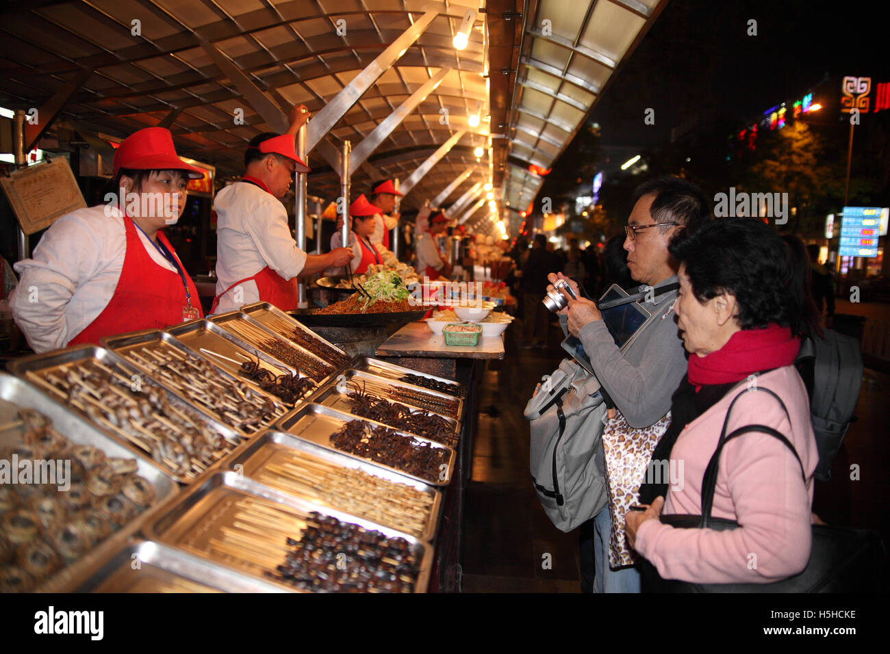 Un couple de touristes chinois, arrêter par un stand de restauration rapide avec brochette de viande, le mari utilise son appareil photo pour prendre des photos. Banque D'Images