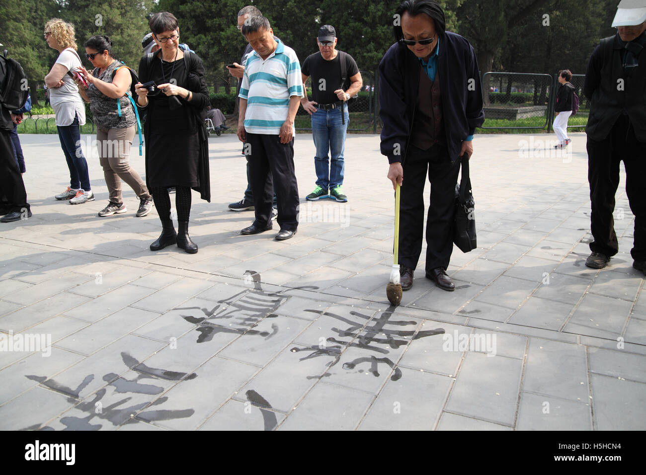 Un Chinois s'amuse à l'aide d'un pinceau et de l'eau énorme à peindre les caractères chinois sur le carrelage par le Temple du Ciel Banque D'Images