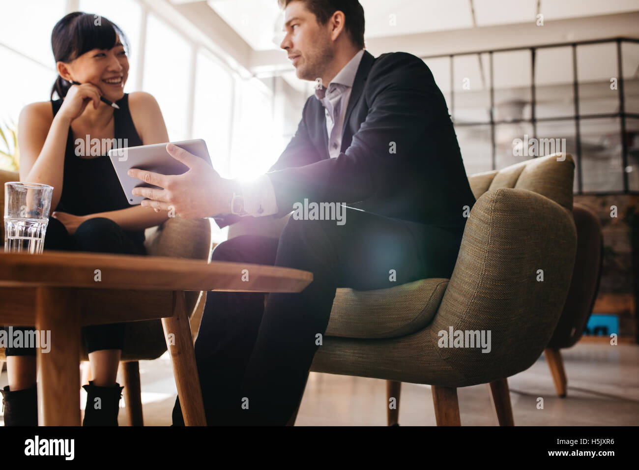 Tiré de deux young businesspeople using digital tablet in lobby of modern office. L'homme et la femme assis sur hall travaillant ensemble Banque D'Images