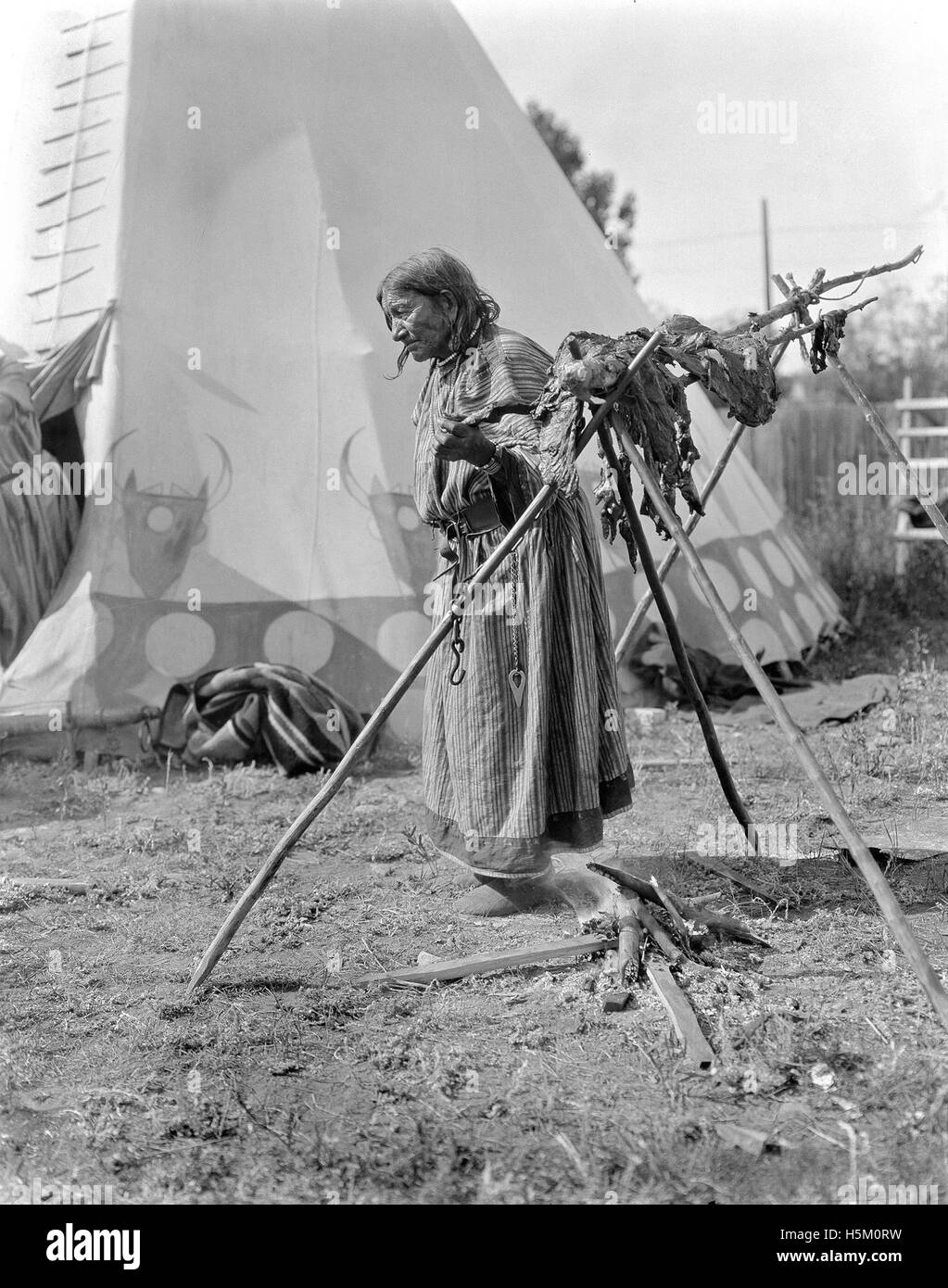 Image d’une femme non identifiée des Premières Nations fumant de la viande, représentant les pratiques autochtones traditionnelles liées à la conservation et à la préparation des aliments. Banque D'Images
