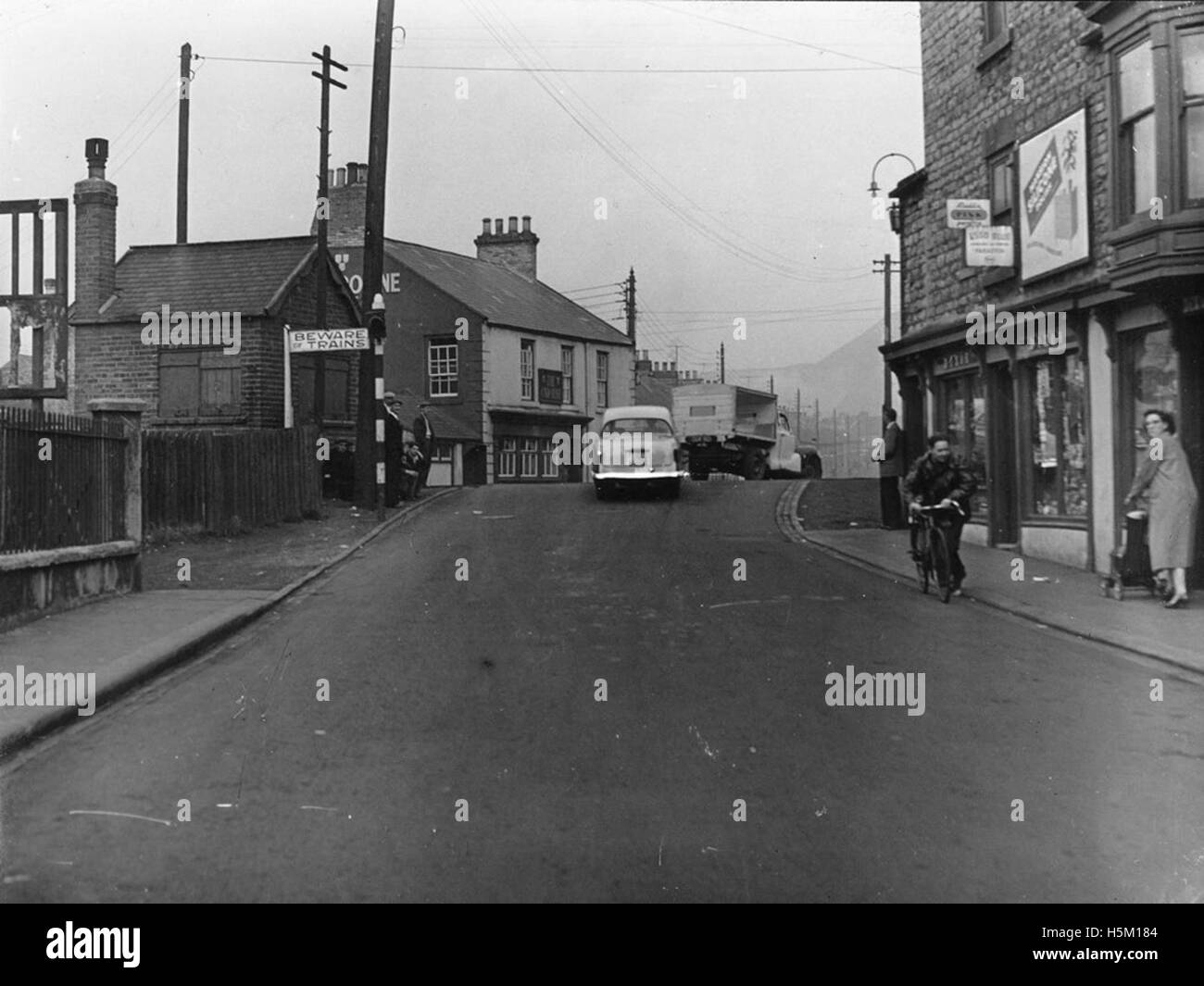 Cette photographie en noir et blanc des années 1950 montre le passage à niveau de la rue Caroline à Hetton-le-Hole, avec piétons, vélos et véhicules. Il capture la vie quotidienne dans la région industrielle, reflétant l'infrastructure et le développement de la région au cours de la période. Banque D'Images