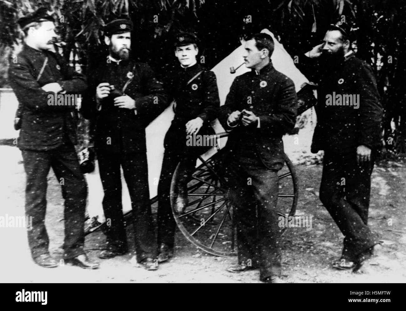 Cette image montre des ambulanciers de Brisbane posant devant une litière sur roues, reflétant les services médicaux d'urgence pendant une période donnée. La tenue vestimentaire des travailleurs et l'équipement mettent en lumière l'histoire du transport médical. Banque D'Images