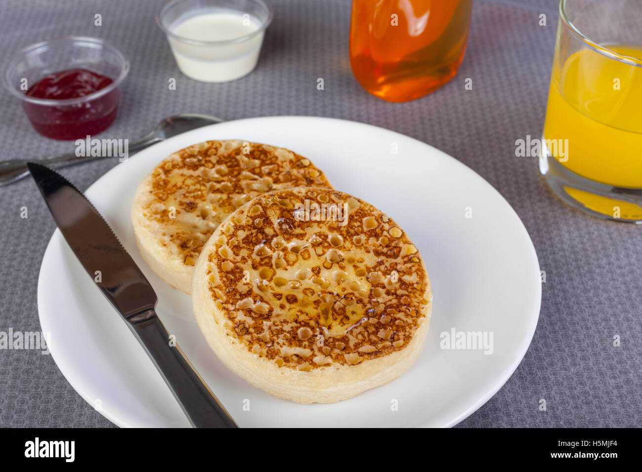 Crumpets sur une plaque avec du sirop d'érable et le jus d'orange sur la table du petit déjeuner Banque D'Images