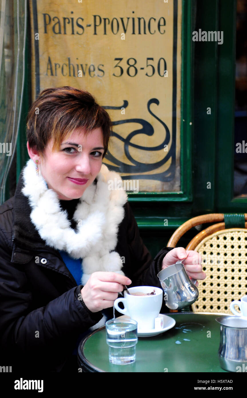 Une jeune femme boit un chocolat chaud à la petite terrasse à l'extérieur au petit fer a cheval dans le quartier du Marais, Paris, France Banque D'Images