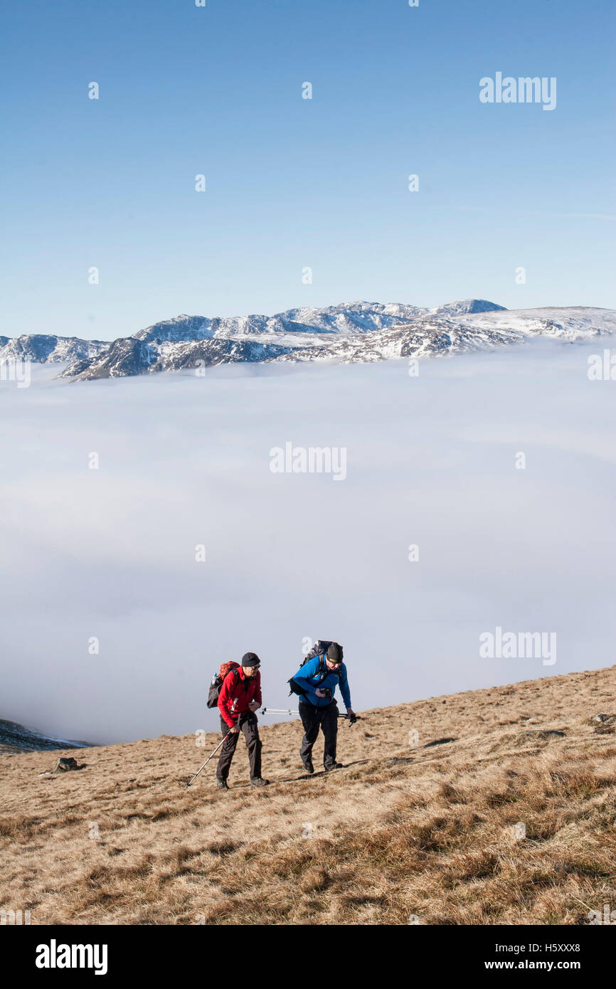 Deux alpinistes grimper hors d'une inversion de température en hiver soleil sur les pentes du grand Rigg, vedette de Fairfield. Banque D'Images