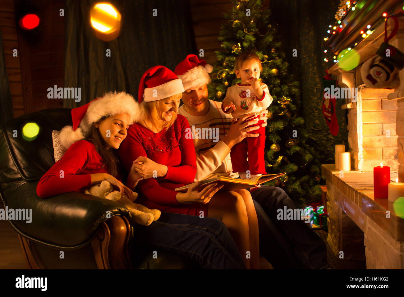 Happy Family sitting on sofa tout en lisant un livre d'histoires dans la décoration de Noël à la maison Banque D'Images